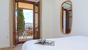 Hotelkamer met een bed, een tijdschrift erop, een grote spiegel en een open deur naar een balkon met een tafel en stoelen.