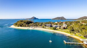 A coastal resort with beachfront villas, a marina, and a view of the ocean and nearby hills. - 9-12 Weatherly Cl - Air Con, Secure parking close to the water (Nelson Bay)