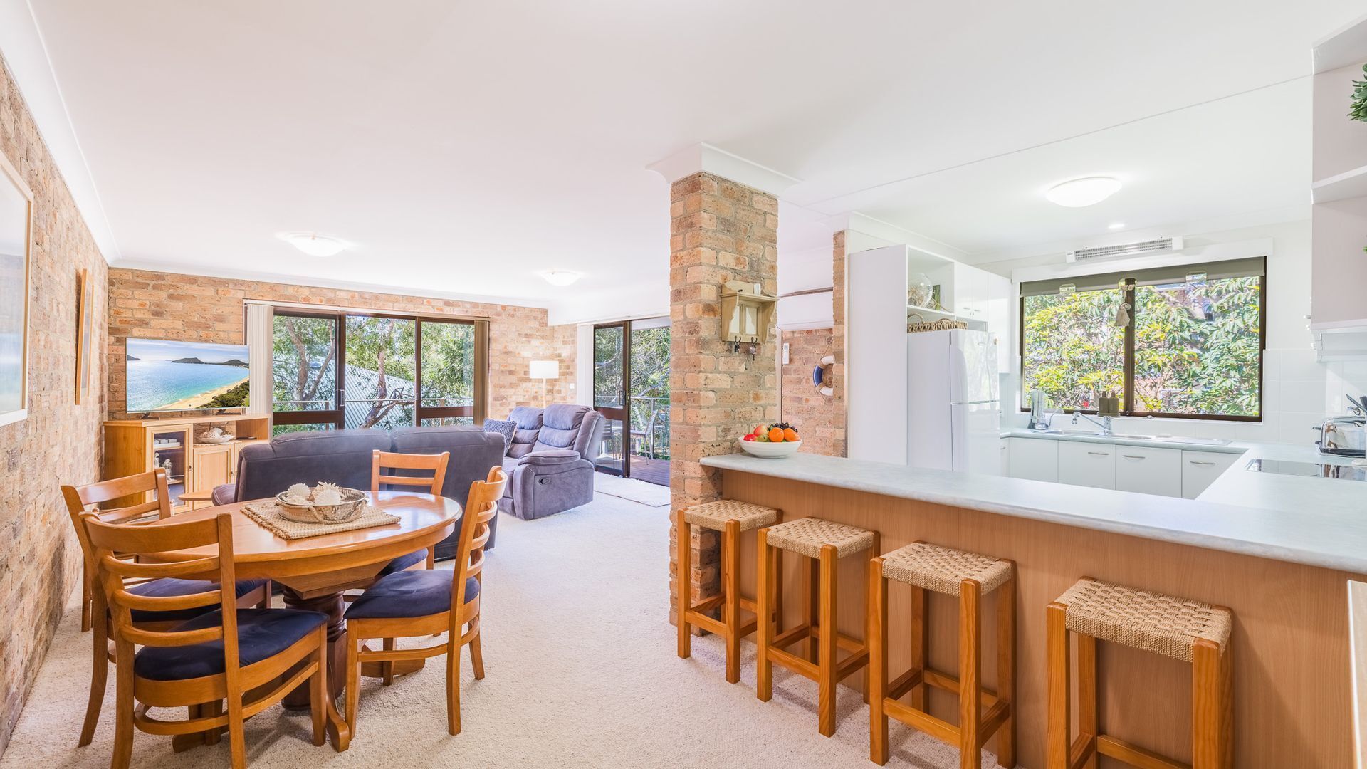 A modern kitchen with a central island, a dining area with wooden chairs, and a living space with a sofa and a TV.