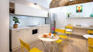 A modern kitchen with white cabinets, a sink, and a dining area with yellow chairs and a table set for breakfast. - Maison Lulu - Naples Old Town (Naples)