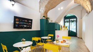 A restaurant interior with yellow chairs, white tables, and a TV displaying a menu. - Maison Lulu - Naples Old Town (Naples)