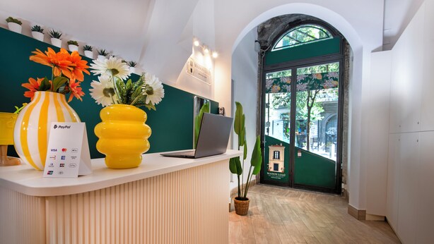A reception desk with a laptop, a PayPal sign, and a vase with flowers. - Maison Lulu - Naples Old Town (Naples)