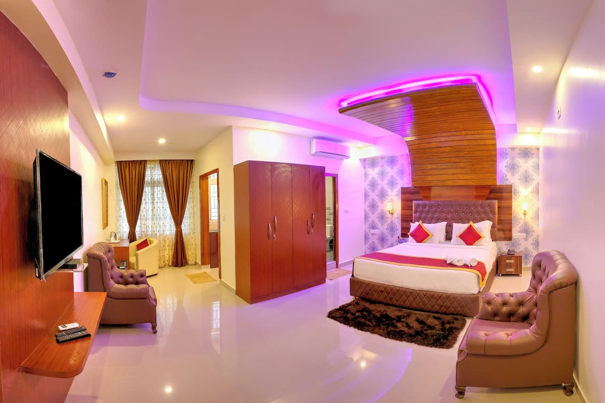 A modern hotel room with a large bed, a sitting area with a sofa and armchair, a flat-screen TV, and a wooden headboard.