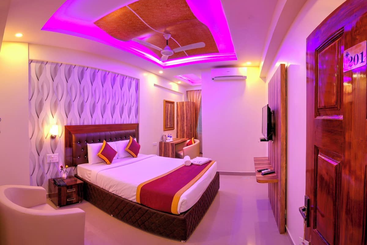 A modern hotel room with a large bed, a ceiling fan, and a wooden door with a number plaque.