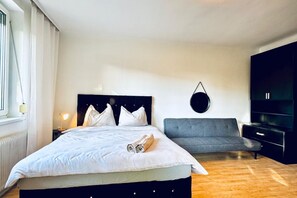 A bedroom with a bed, bedside table, lamp, grey sofa, and a black wardrobe.