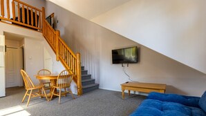 A living room with a staircase, a dining table with chairs, a blue sofa, and a flat-screen TV mounted on the wall. - 5 Mins from the Resort | Sleeps 3 | Dog Friendly (Fernie)