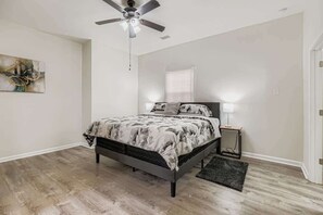 A bedroom with a bed, a ceiling fan, a nightstand, a lamp, and a painting on the wall.