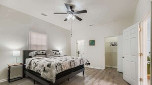 Une chambre à coucher comprenant un lit, un ventilateur de plafond, une table de chevet et un dressing.
