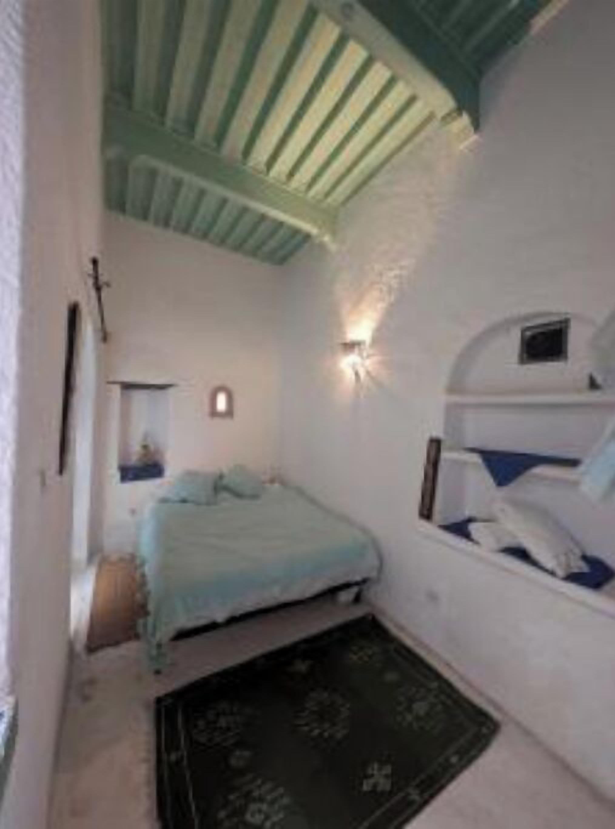 A small, cozy bedroom with a single bed, a nightstand, a wall-mounted light, and a ceiling fan.