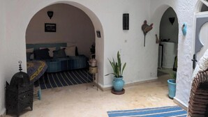A room with a bed, a small table, and a potted plant. There are two arches leading to another room. - RIAD MEDINA (Essaouira)