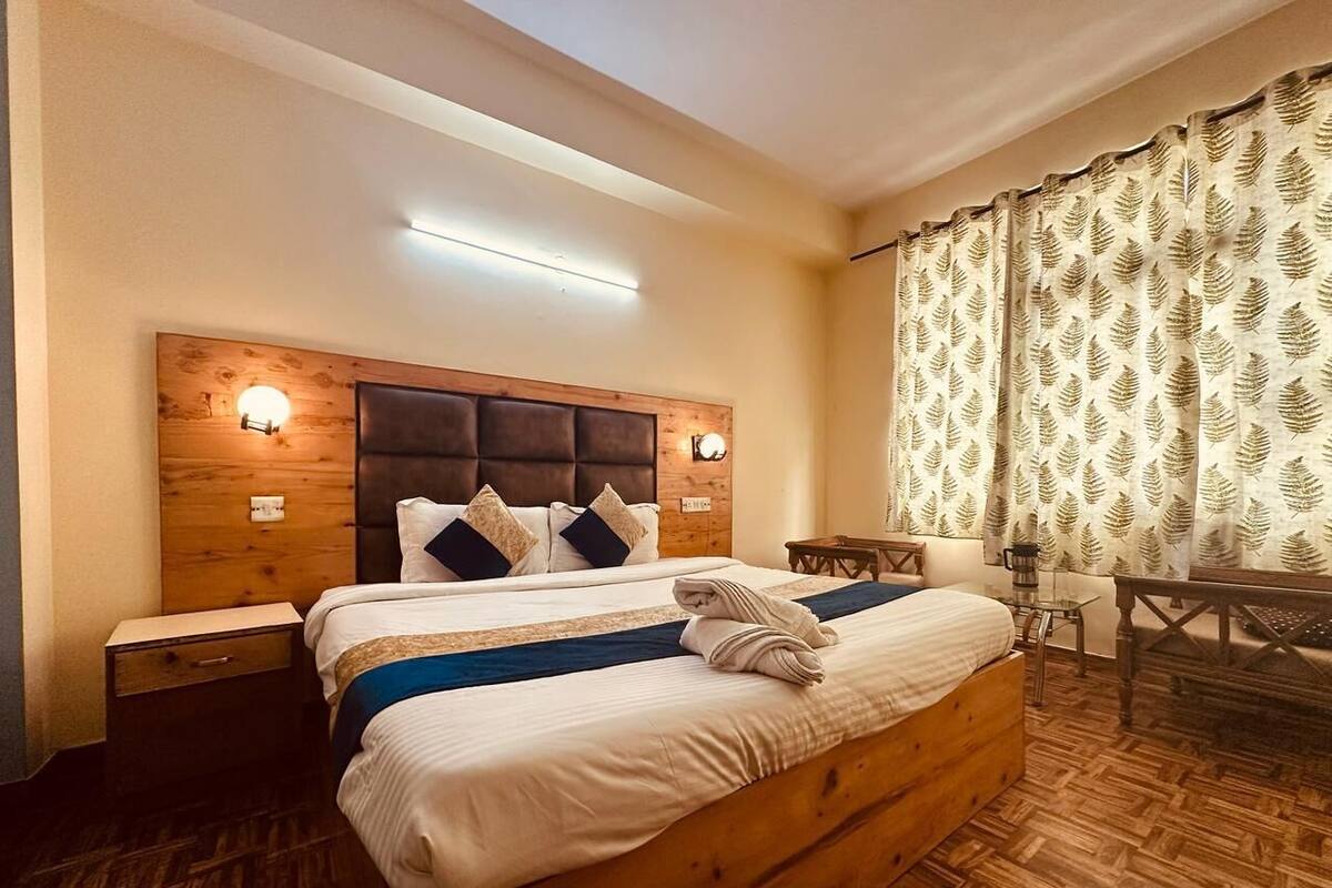 A hotel room with a wooden bed, two bedside tables, a desk, and a patterned curtain.