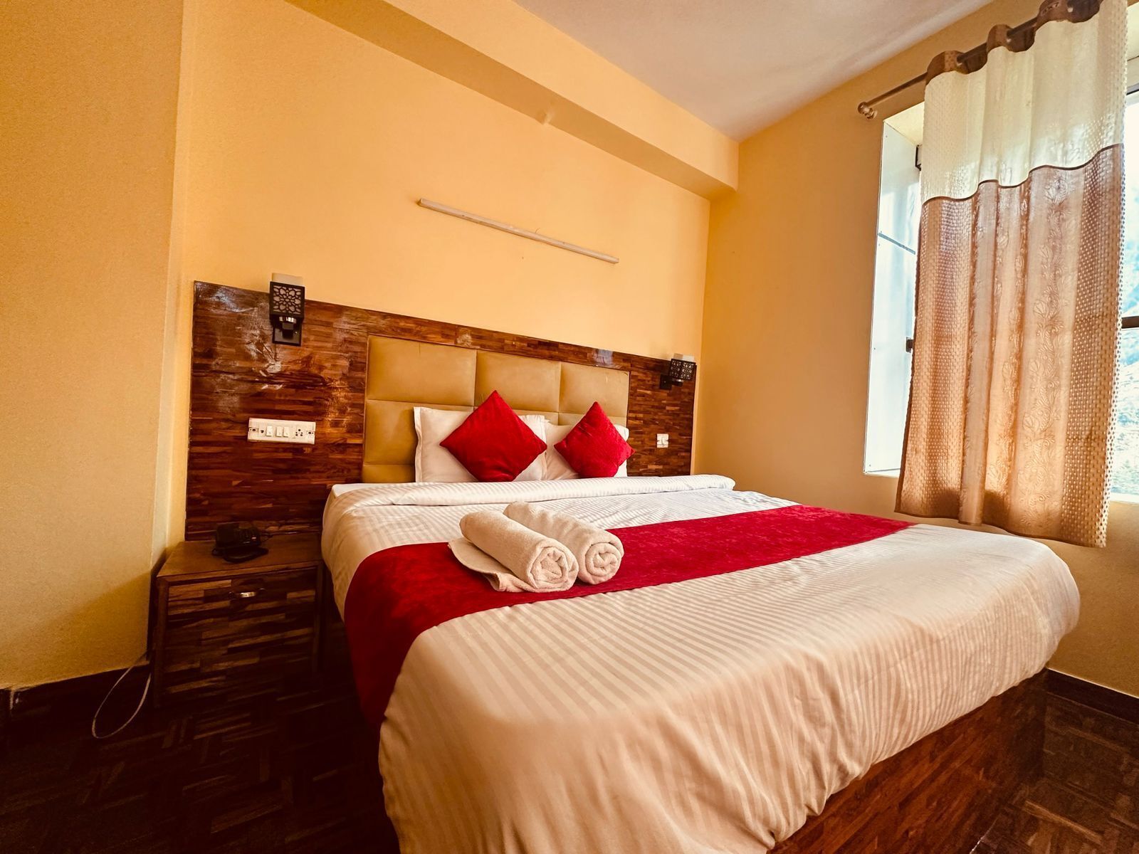 A neatly made bed with a red and white bedspread, a wooden headboard, and a nightstand with a lamp.