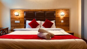 A neatly made bed with a red blanket, two red pillows, and a rolled towel on a wooden headboard with wall-mounted lights. - The Kanchanikoot (Manali)