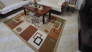 A living room with a sofa, a coffee table, a rug, a chandelier, and a TV. - Lakeside View Apartment (Udënisht)