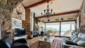 A cozy living room with stone walls, a fireplace, a large TV, and a sofa. - Charming villa just 10 minutes (800m) walk from Palombaggia Beach (Porto-Vecchio)