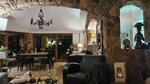 A stone-walled living room with a chandelier, a fireplace, and a dining area. - Charming villa just 10 minutes (800m) walk from Palombaggia Beach (Porto-Vecchio)