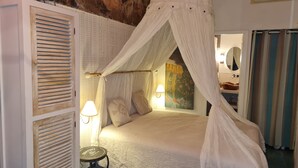 A bedroom with a canopy bed, a stone wall, a small table, and a painting. - Charming villa just 10 minutes (800m) walk from Palombaggia Beach (Porto-Vecchio)