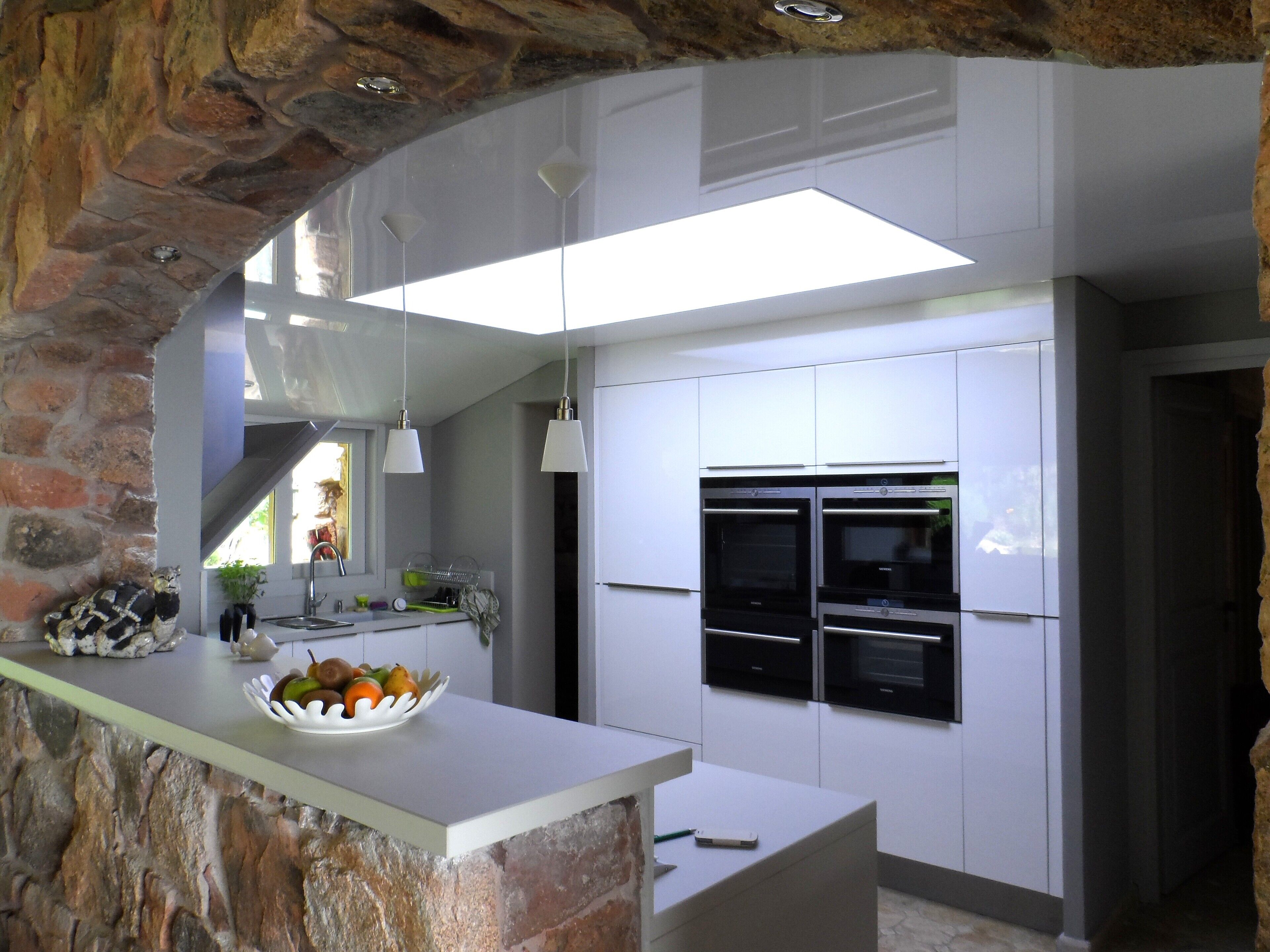 A modern kitchen with white cabinetry, two built-in ovens, a white countertop, and a stone accent wall.