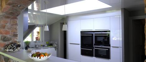 A modern kitchen with white cabinetry, two built-in ovens, a white countertop, and a stone accent wall.