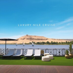 Une terrasse avec des chaises longues et des poufs, une vue sur l’eau et une colline de sable en arrière-plan.