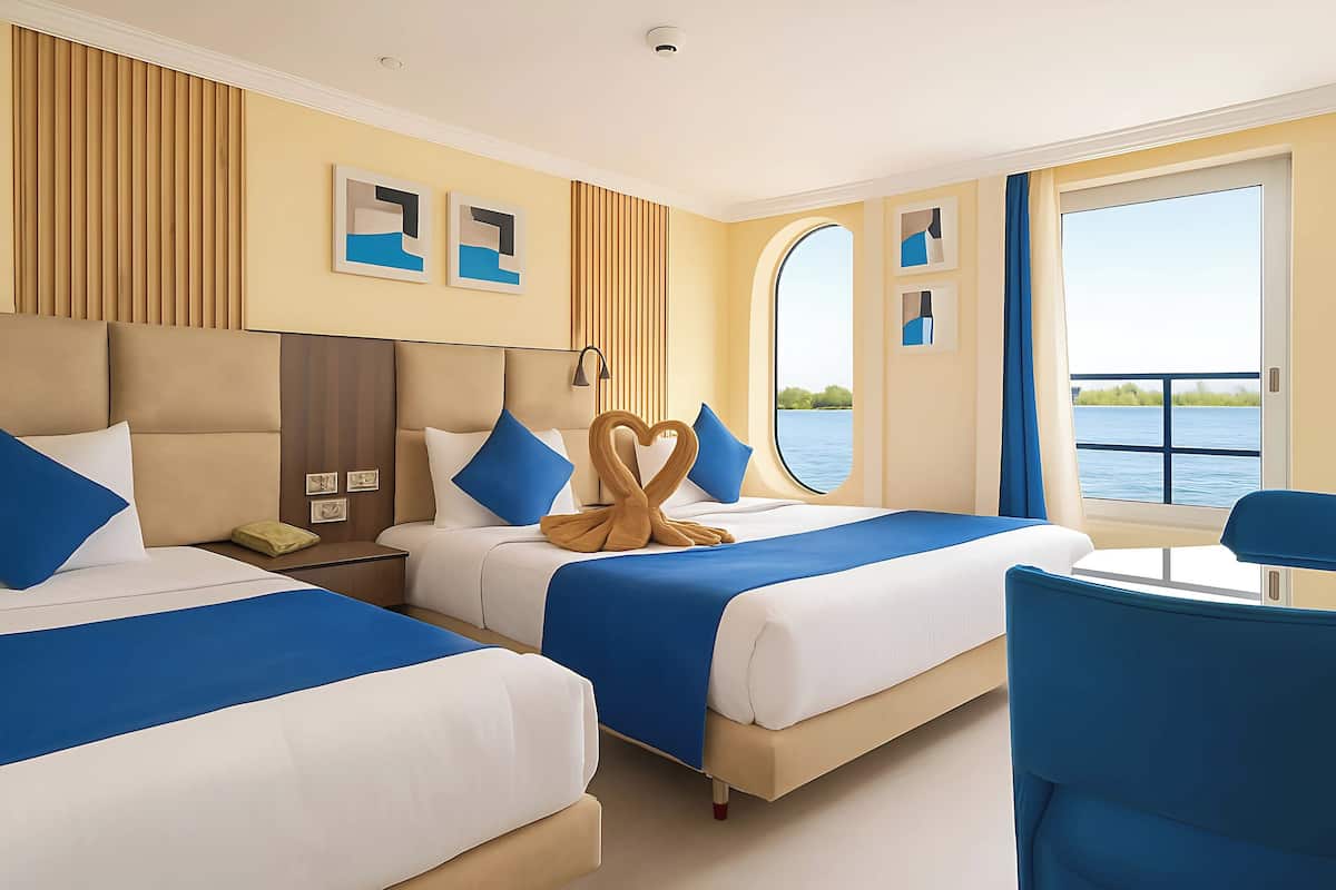 Een hotelkamer met twee bedden, een bureau en uitzicht op het water.