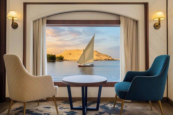 Ein Zimmer mit zwei Stühlen und einem Tisch, ein großes Fenster mit Vorhängen und Blick auf ein Segelboot auf dem Wasser.
