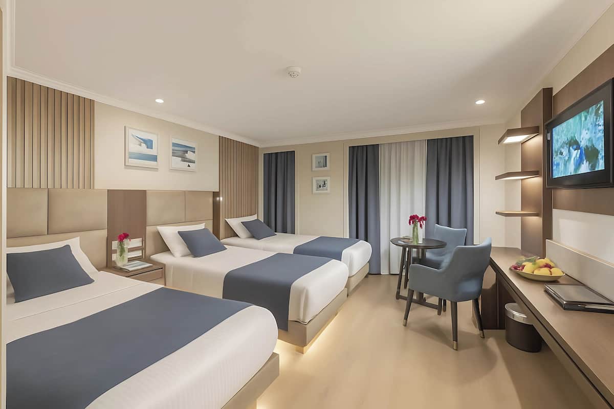 Een hotelkamer met twee bedden, een bureau, een stoel, een televisie en een klein tafeltje met fruit.