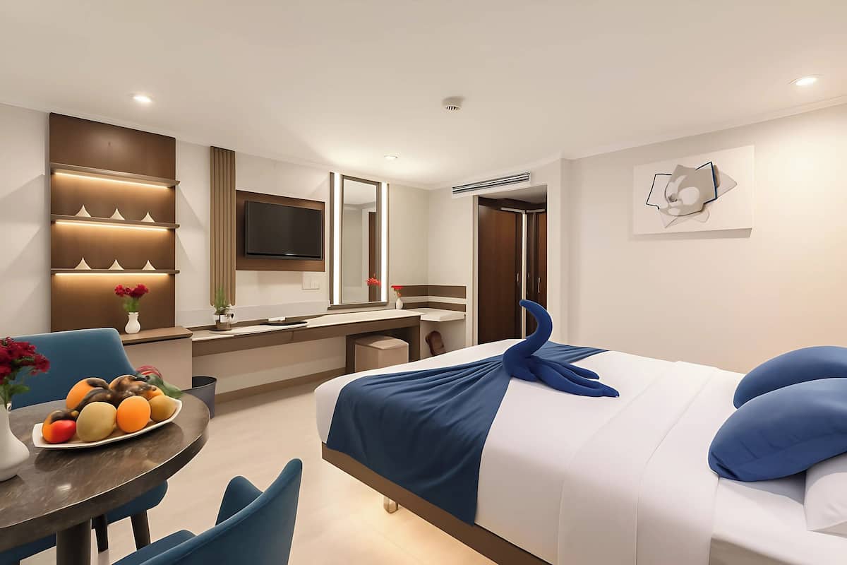 Een moderne hotelkamer met een bed, bureau, stoel, eettafel met fruit en een televisie.