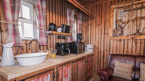 A rustic kitchen with wooden walls, a white sink, a coffee maker, and a flour container. - Rusty Barn (Limavady)