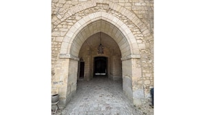 Un arc en pierre mène à un bâtiment dont le sol est pavé de pierres.