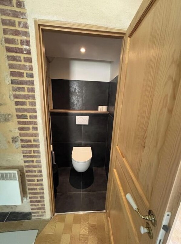 Een kleine, smalle badkamer met een toilet, een plank boven het toilet en een houten deur.