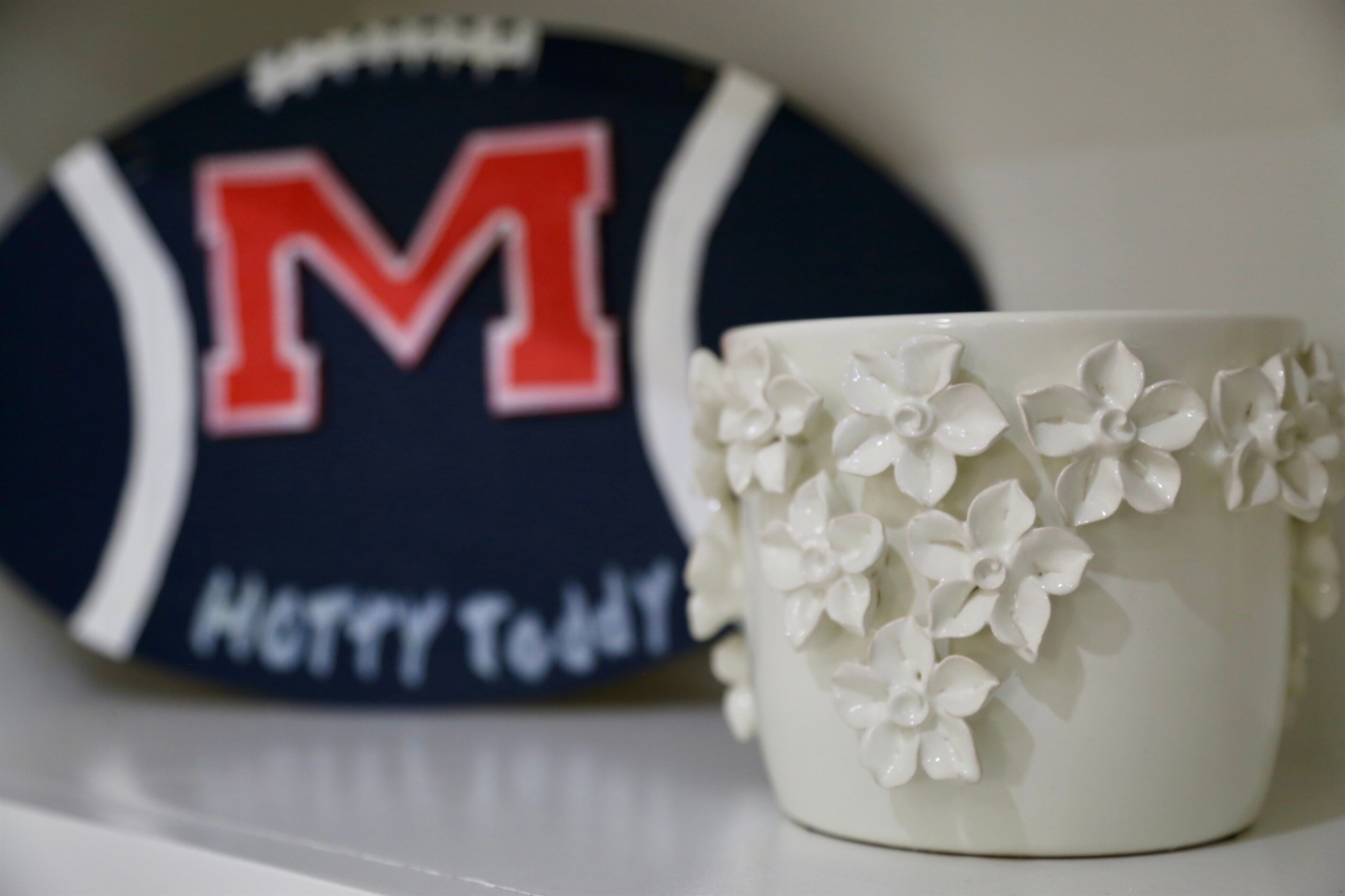 Eine weiße Tasse mit floralen Mustern und ein sportlicher Untersetzer mit einem großen roten 'M' und der Aufschrift 'Happy Teddy'.