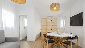 A modern living room with a round dining table, wooden chairs, a grey sofa, and a TV mounted on the wall. - Vallecano Apartments by Olala Homes (Madrid)