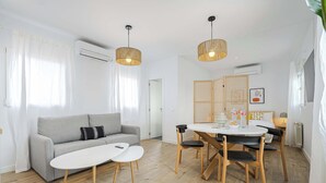 A modern living room with a grey sofa, a small white table, and a dining area with a wooden table and chairs. - Vallecano Apartments by Olala Homes (Madrid)
