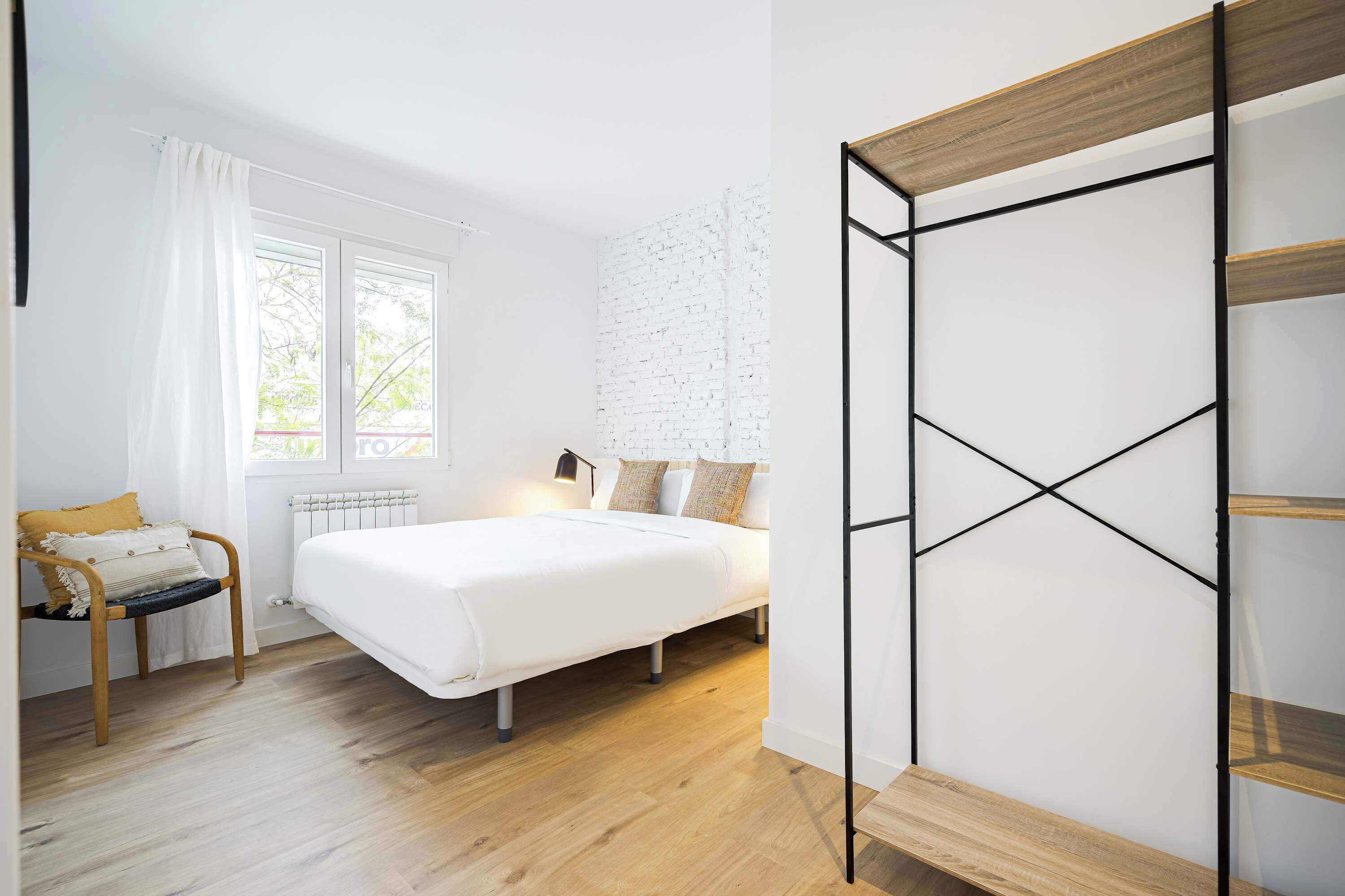 A bedroom with a bed, a chair, a wooden bench, and a white brick wall.