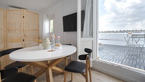 A modern dining area with a round table, black chairs, and a view of a waterfront through a large window. - Vallecano Apartments by Olala Homes (Madrid)