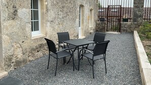 A stone building with a gravel patio, a table with four chairs, and a metal gate in the background.