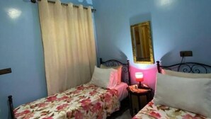 A bedroom with two beds, a nightstand with a lamp, a mirror, and a window with curtains. - Furnished apartment with 2 bedrooms, kitchen, bathroom and living room (Meknès)