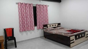 A bedroom with a bed, a chair, and a window with curtains. - Hotel Jijau Darbar (Mahād)