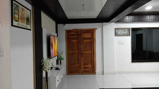 A hallway with a wooden door, a framed picture, and a potted plant. - Hotel Jijau Darbar (Mahād)