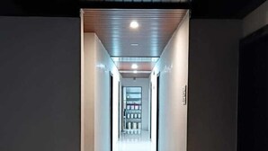 A long, narrow hallway with a reflective floor leading to a brightly lit room at the end. - Hotel Jijau Darbar (Mahād)