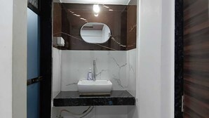 A bathroom with a white sink, a mirror, and a marble backsplash. - Hotel Jijau Darbar (Mahād)
