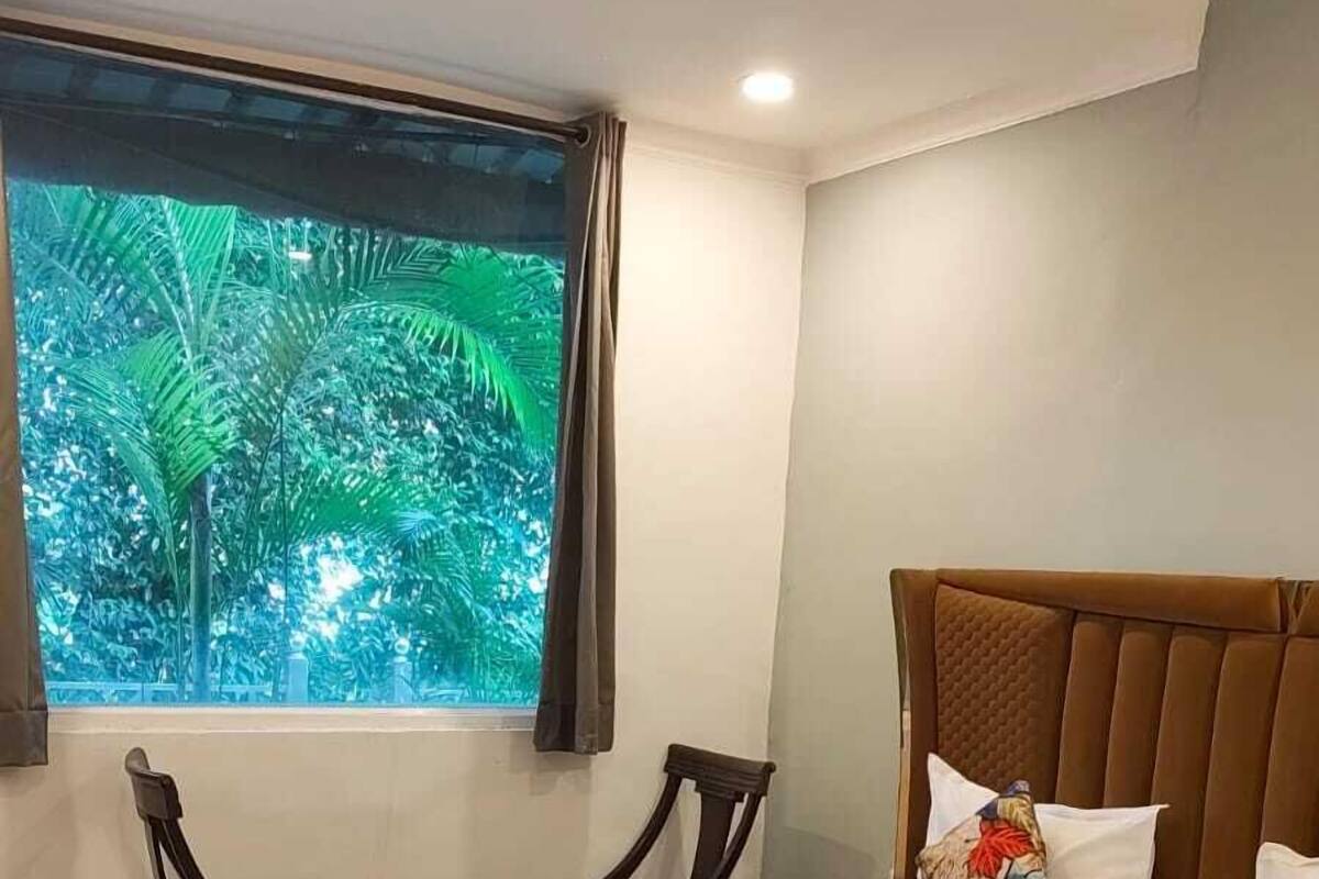 A bedroom with a bed, a window with a view of greenery, a ceiling fan, and a bedside table.