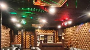 A bar area with leather seating, a bar counter, and a ceiling with green and red lights. - Haveli NH 8 (New Delhi)