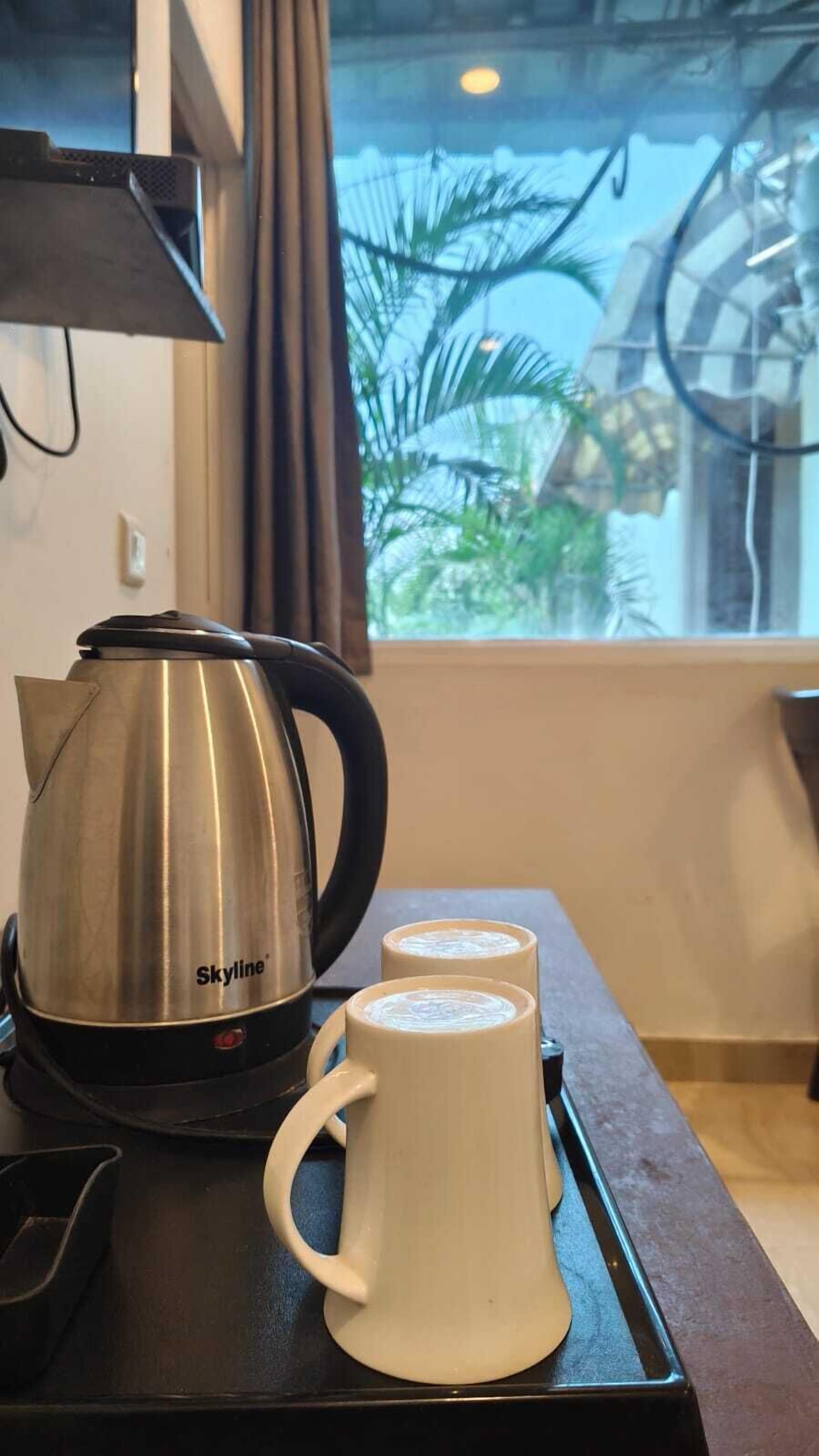 Een kitchenette met een roestvrijstalen waterkoker en twee witte mokken op een dienblad.