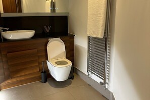 A modern bathroom with a white toilet, a vessel sink, and a towel rack. - Exclusive 2 Bedroom Apartment (London)