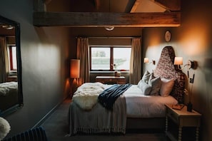 Ein Schlafzimmer mit einem großen Bett, einem Nachttisch, einem Spiegel, einem Fenster mit Vorhängen und Blick ins Freie.