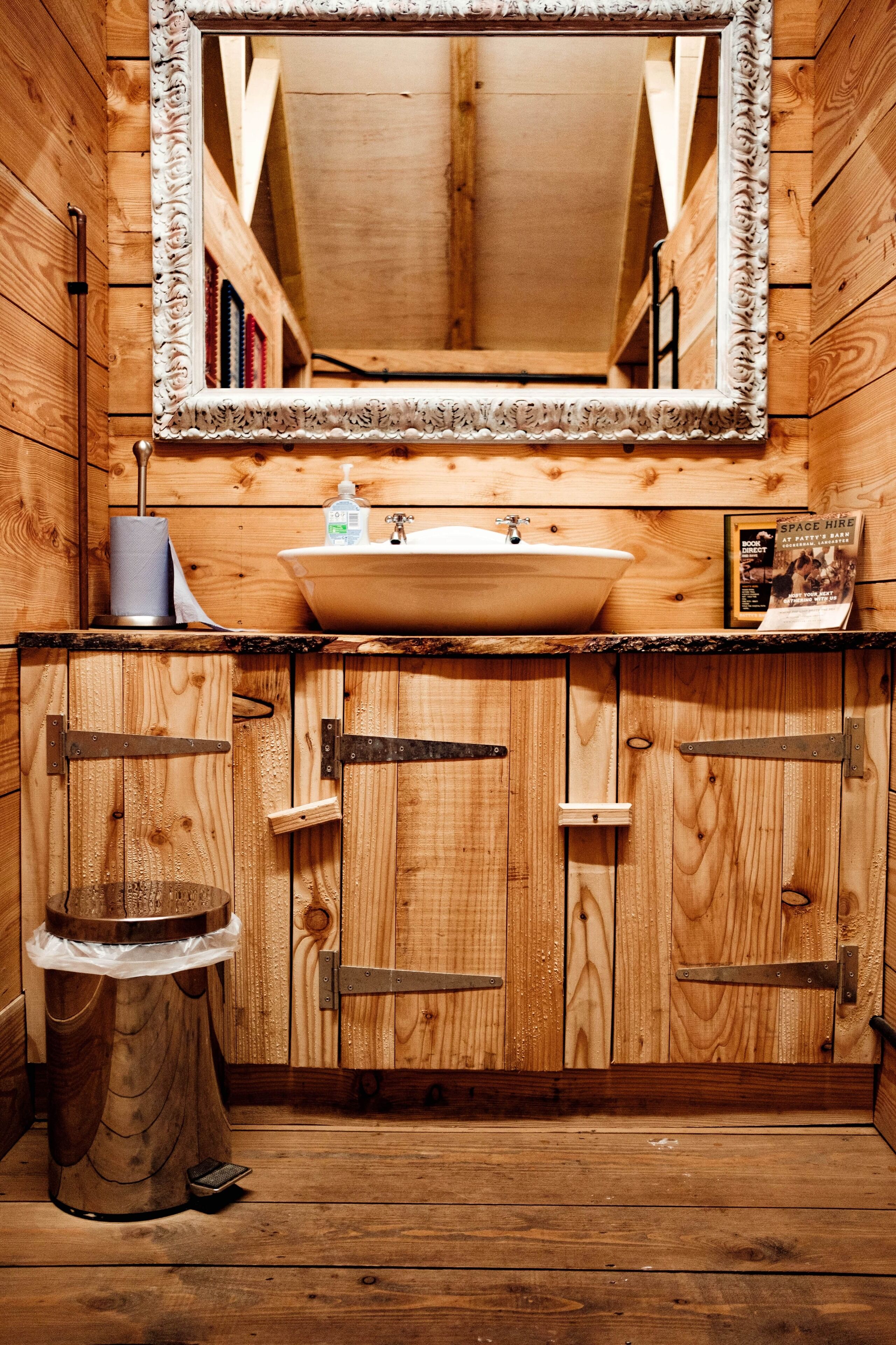 A wooden cabin-style bathroom with a large mirror, wooden cabinets, a sink, and a toilet.