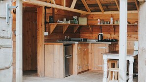 A wooden cabin with a kitchen area featuring a refrigerator, a coffee maker, and shelves with various items. - Mushroom Hut at Patty's Barn (Lancaster)