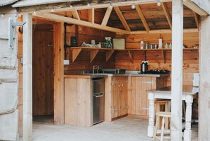 A wooden cabin with a kitchen area featuring a refrigerator, a coffee maker, and shelves with various items.